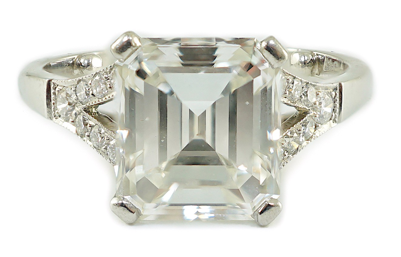 A platinum and single stone emerald cut diamond ring, with brilliant cut diamond set split shoulders